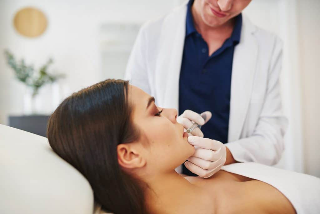 Doctor injecting botox into a young female client's lip